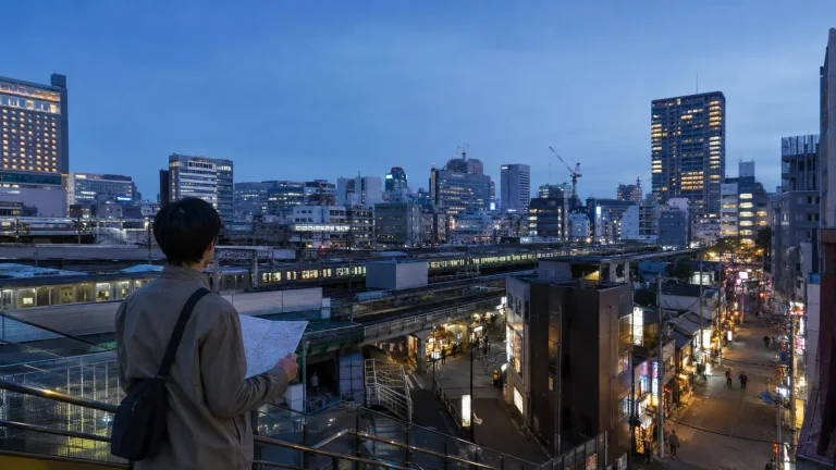 Traveler planning a three-day Tokyo itinerary above city rail lines at dusk