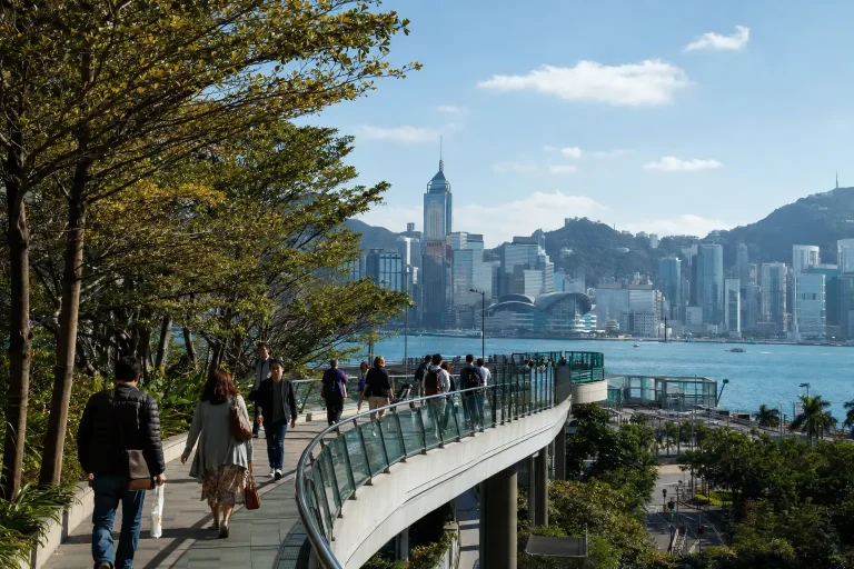 Pedestrians walking beside Victoria Harbour on a clear late-autumn day in Hong Kong