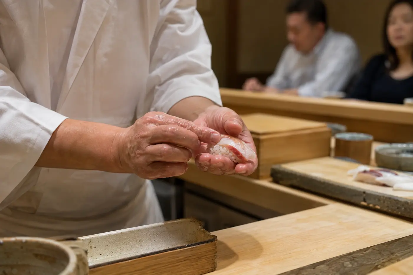 Chef shaping Edomae nigiri sushi at a pale wood Tokyo counter
