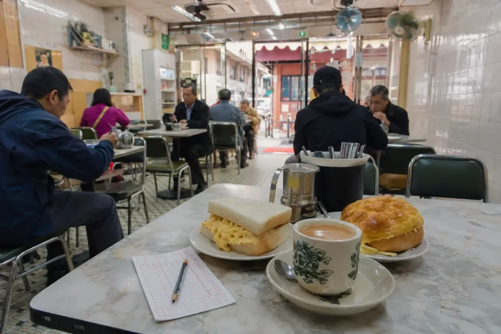 Milk tea, an egg sandwich and a pineapple bun on a table inside a Hong Kong cha chaan teng