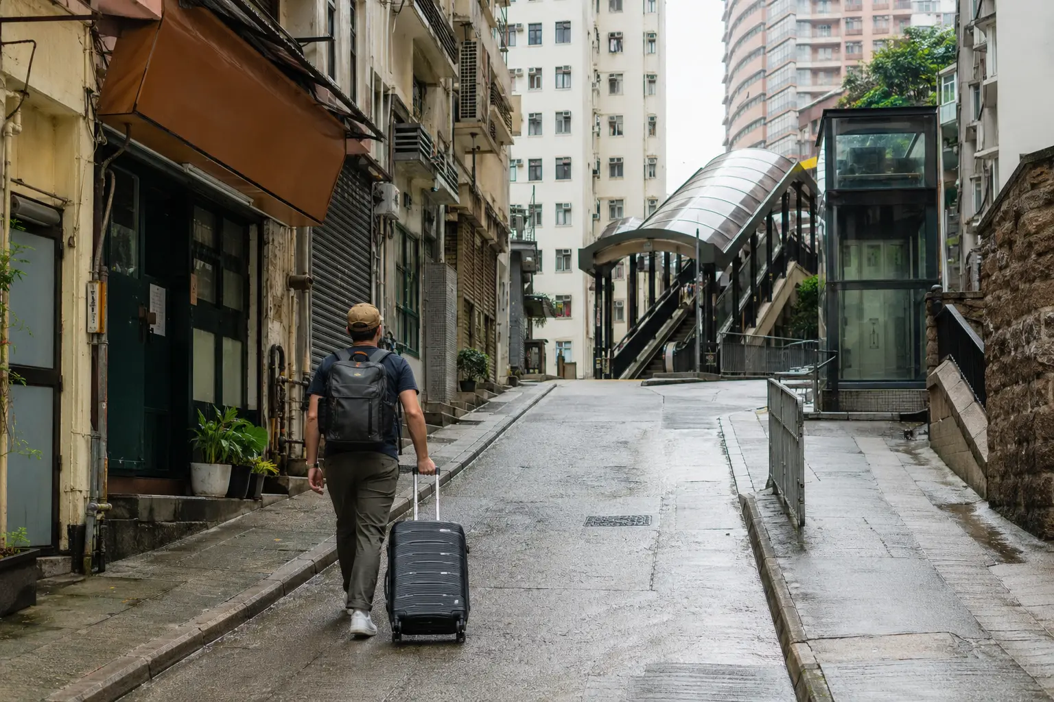 Traveler pulling a suitcase uphill toward an escalator and public lift in Hong Kong