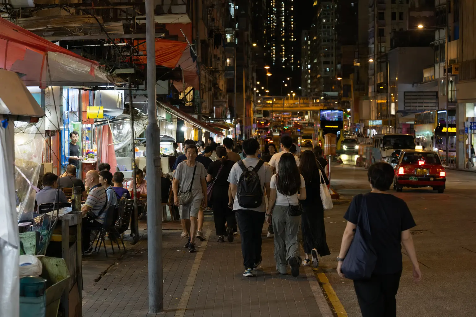 People walking past late-night food stalls and buses in Jordan, Hong Kong