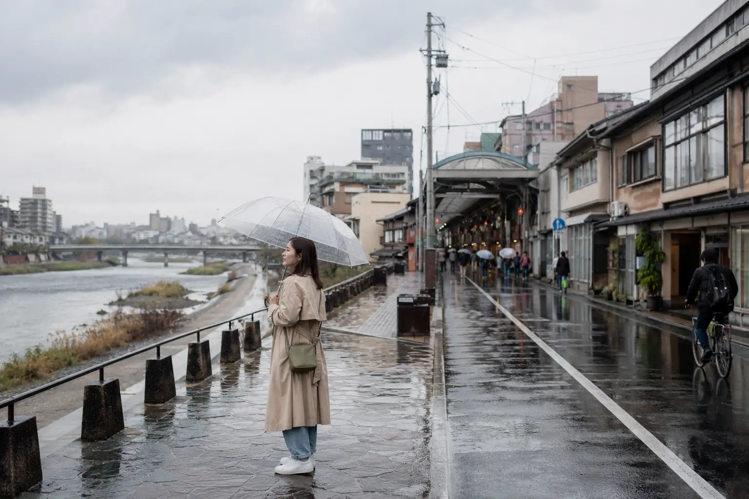 Traveler with a clear umbrella beside the Kamo River on a rainy Kyoto afternoon