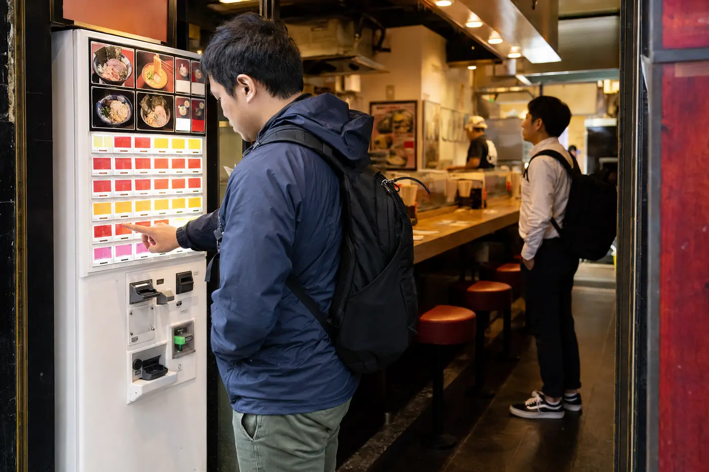Solo diner selecting ramen from a ticket machine at a Tokyo noodle shop