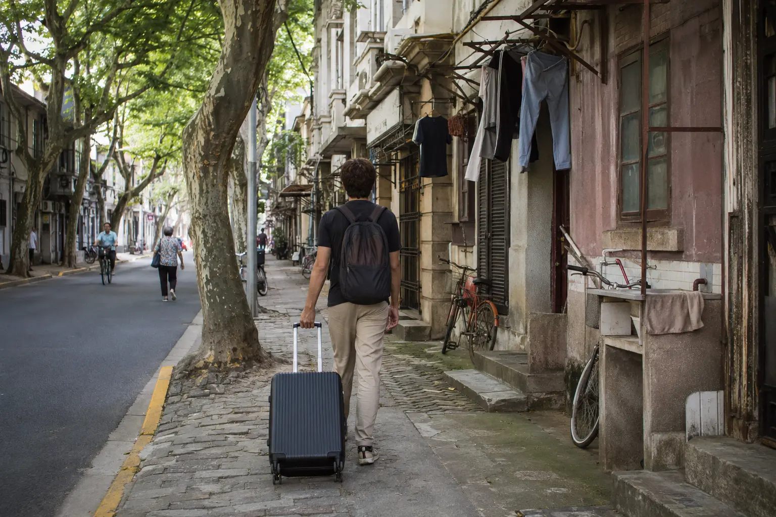 Traveler rolling a suitcase along a leafy residential street in Shanghai's former French Concession