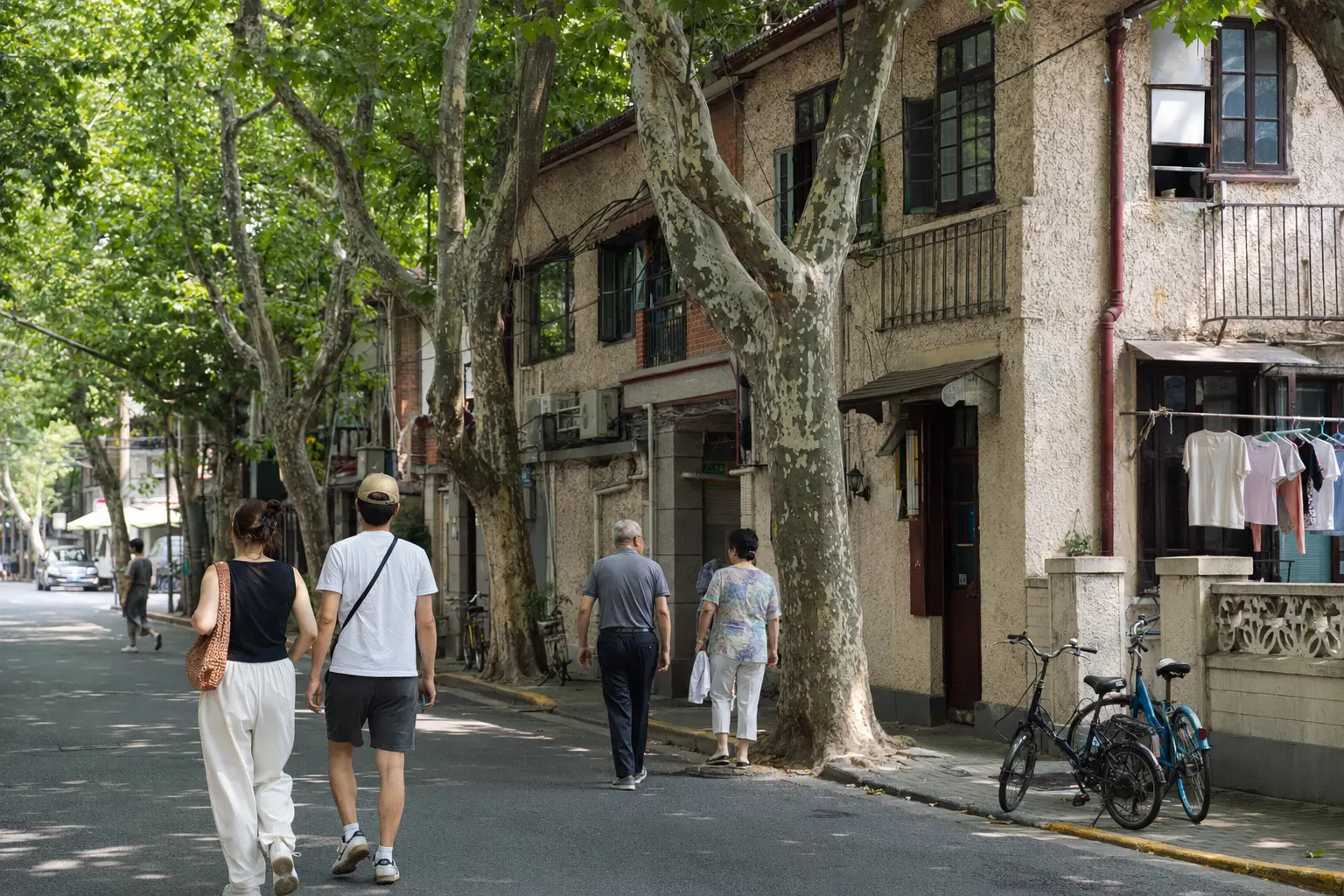 Travelers walking past lane houses beneath plane trees in Shanghai