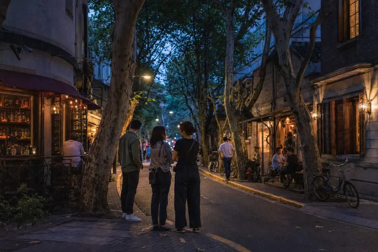 Friends choosing between small bars on a tree-lined Shanghai street at blue hour