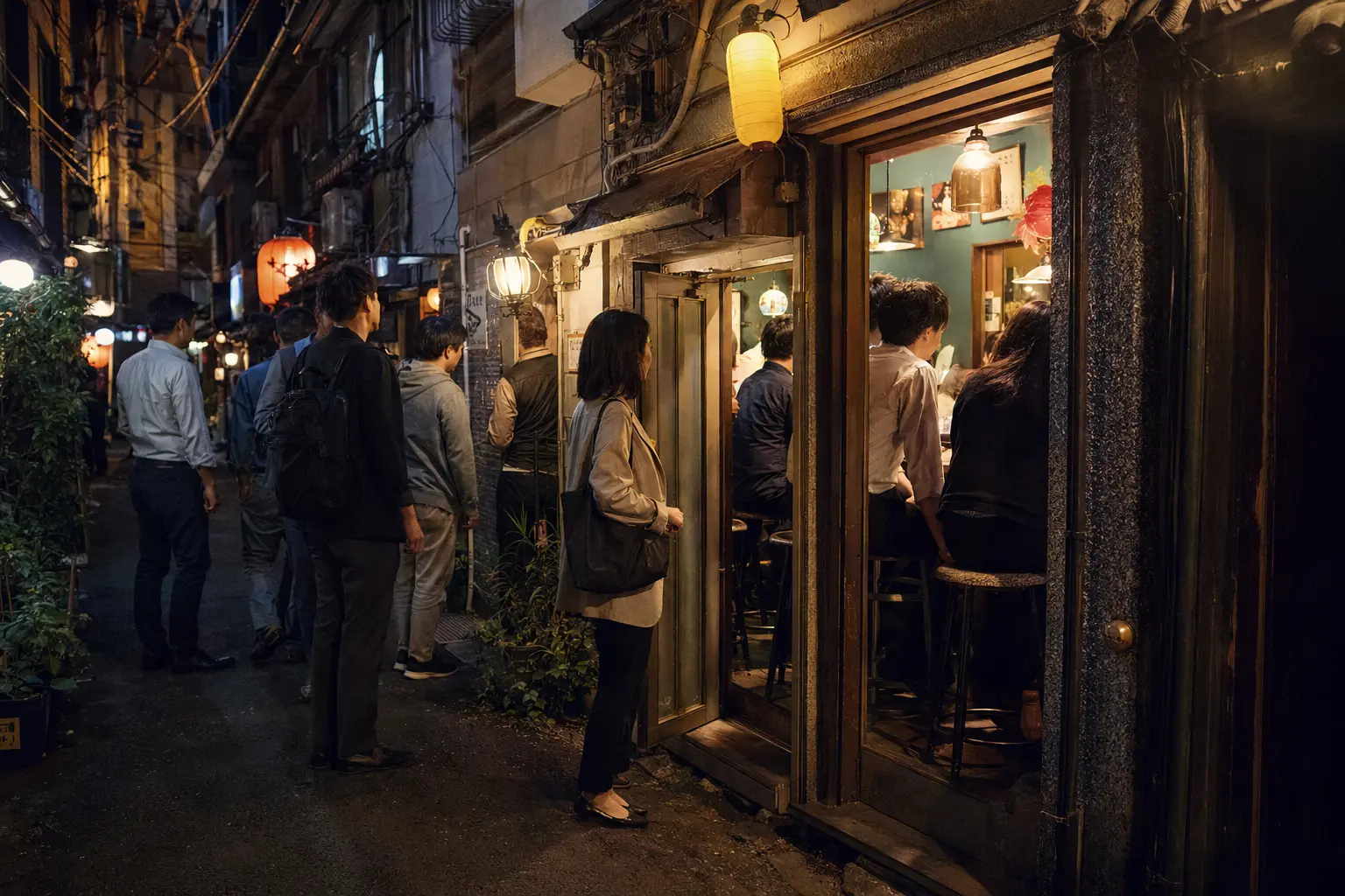 Patrons choosing a tiny bar in a narrow Shinjuku yokocho at night