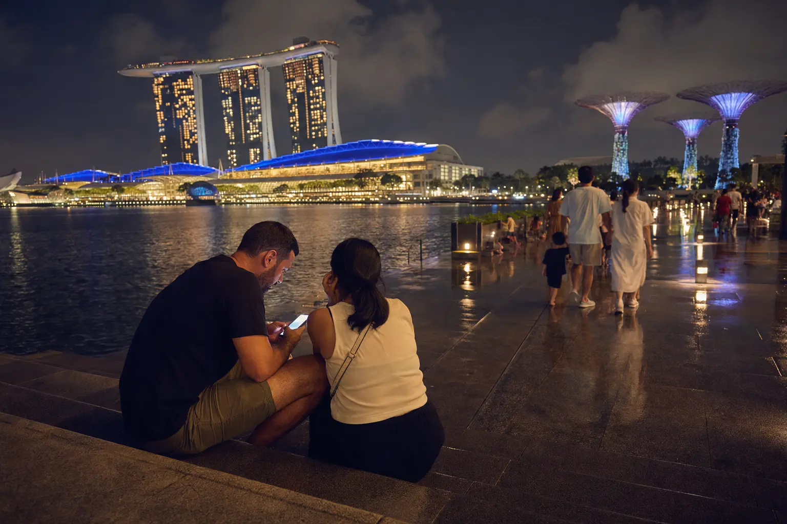 Travelers planning their MRT return beside Marina Bay at night