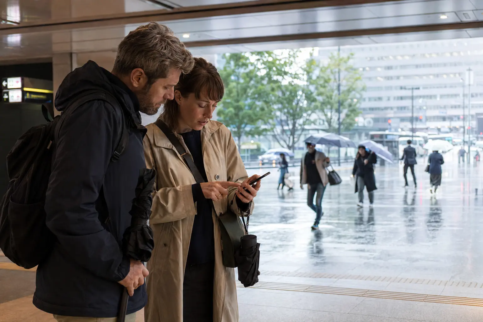 Travelers adjusting their Tokyo itinerary on a rainy day outside a covered station entrance