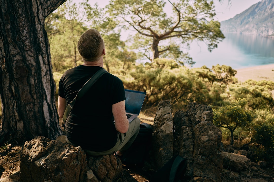 Man inspiring for a work inside the mountains. Sitting on the rock and working online — The Complete Guide to Digital Nomad Visas: Compare 12+ Countries
