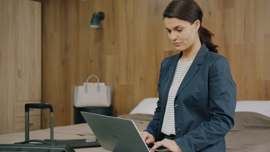 Young woman in formal clothing is using laptop working online in hotel room, suitcases and modern room visible in background. People and business trip concept. — How to Become a Digital Nomad: A Complete Beginner’s Guide