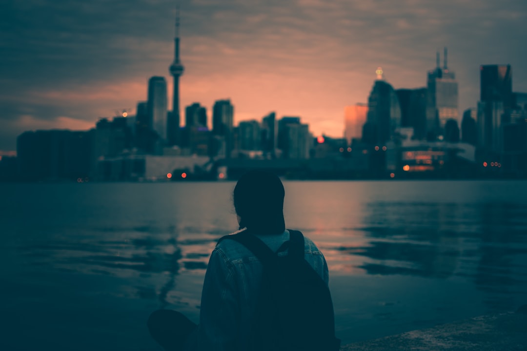 person with backpack sitting near body of water with buildings ahead — How to Be More Self-Disciplined (Even When Motivation Runs Out)