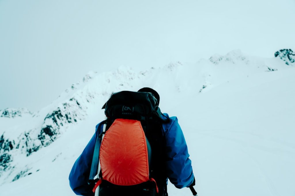 Hiker with orange backpack ascends a snow-covered mountain — ski trip packing list