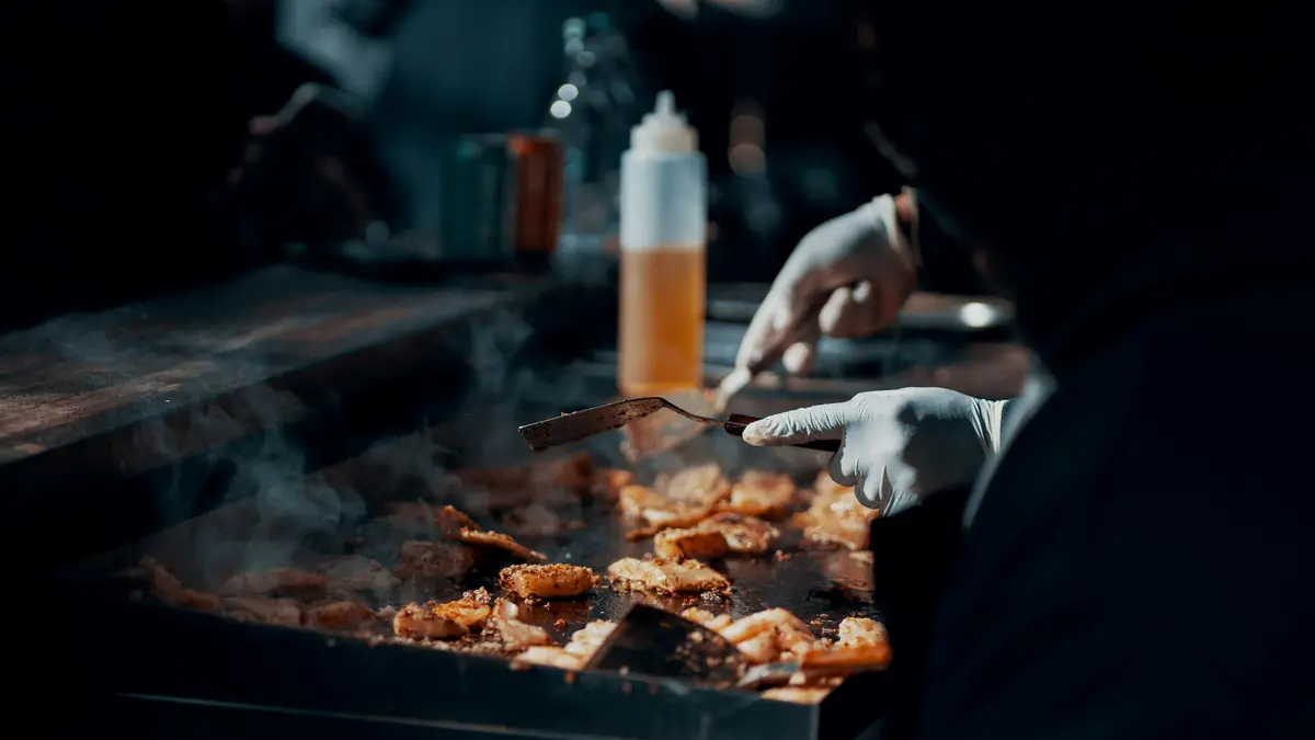 Gloved hands turning pieces of food on a smoky flat-top grill at Borough Market