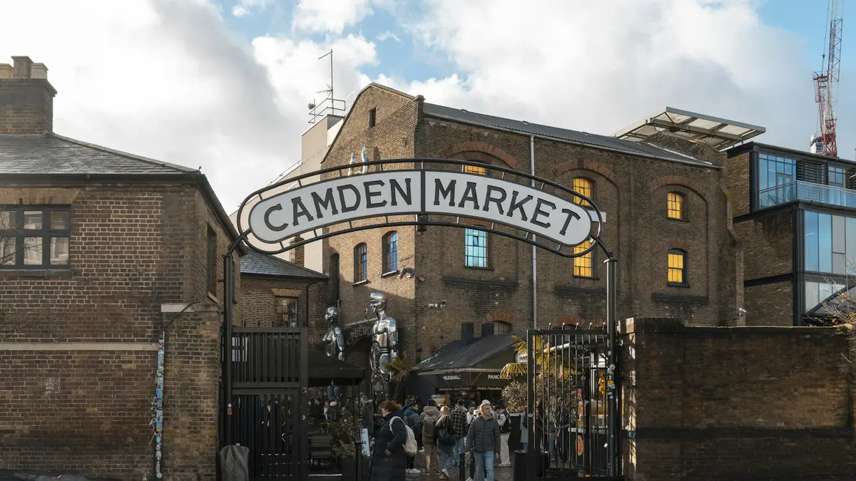 People walking beneath the large Camden Market entrance sign between brick buildings
