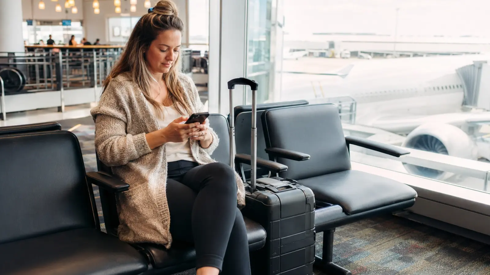 Traveler with a carry-on checking her phone at a quiet airport gate