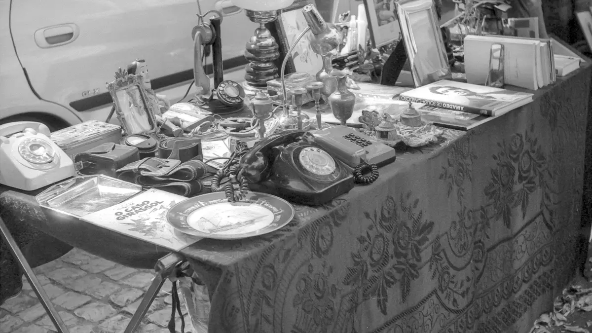 Rotary telephones, lamps, books and small vintage objects arranged on a table at Feira da Ladra in Lisbon