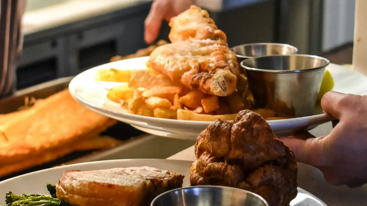 Fish and chips behind a plate of roast pork, greens and Yorkshire pudding on a kitchen pass