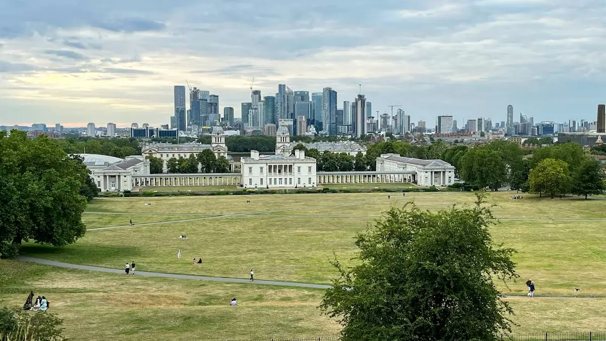 Greenwich Park lawns and historic buildings with the Canary Wharf skyline in the distance