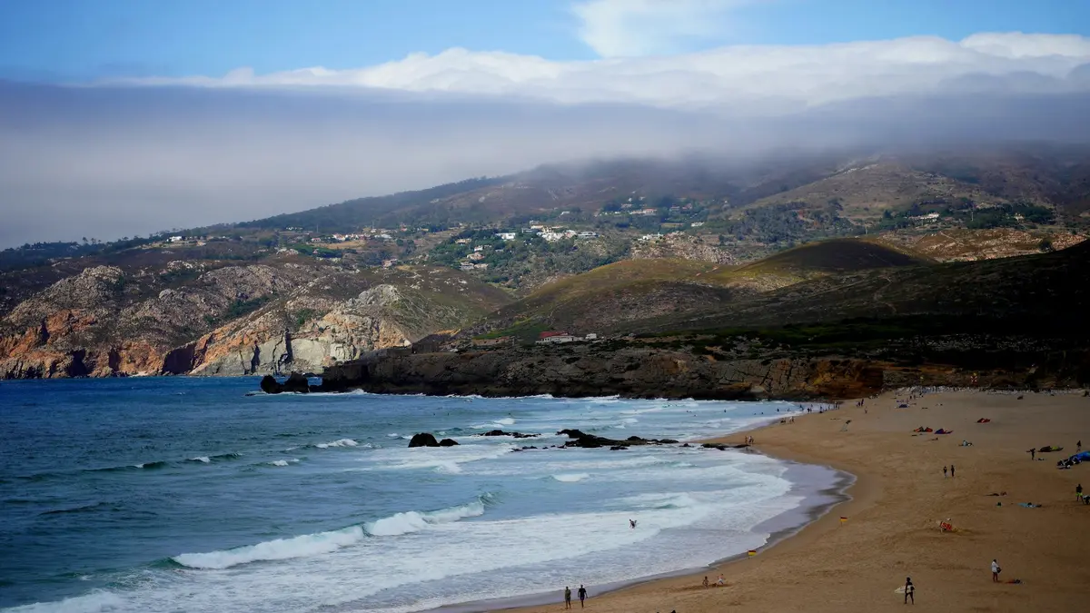 People on sandy Guincho Beach below mist-covered coastal hills and Atlantic waves