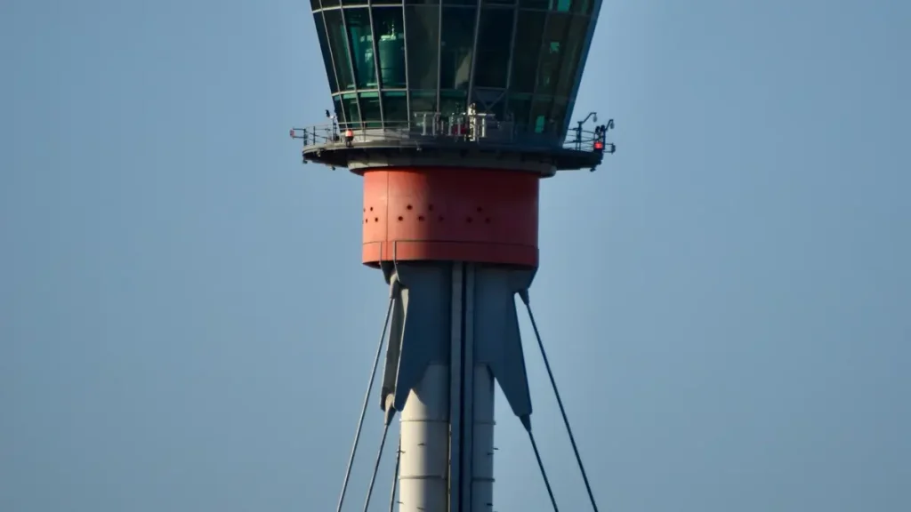 Close-up of Heathrow Airport's red-and-grey air traffic control tower against a blue sky