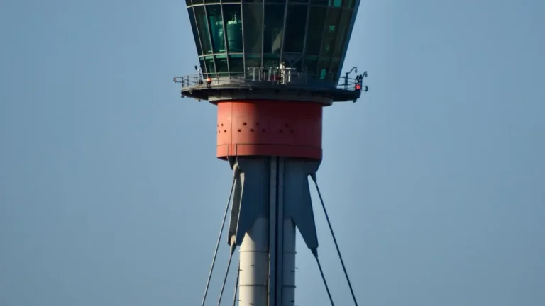 Close-up of Heathrow Airport's red-and-grey air traffic control tower against a blue sky