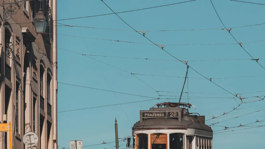 Historic Tram 28 beneath overhead wires on a bright Lisbon street