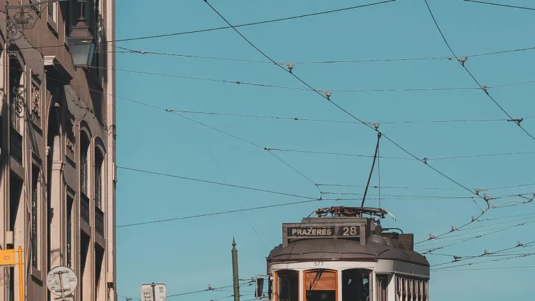 Historic Tram 28 beneath overhead wires on a bright Lisbon street