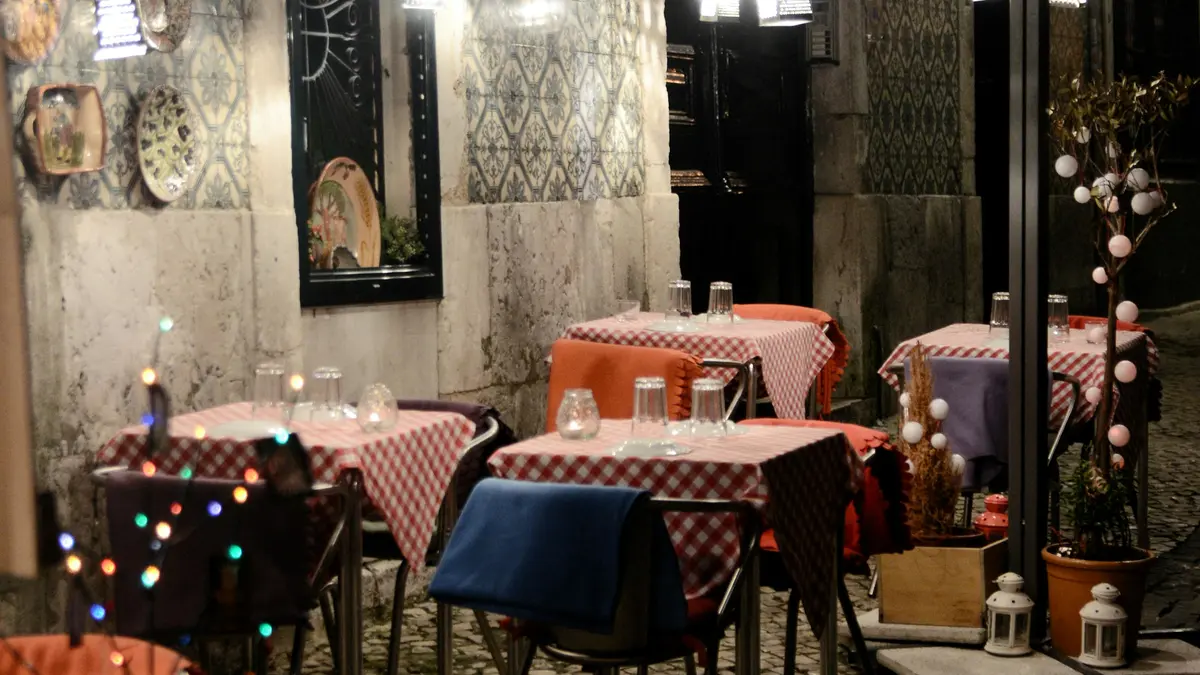 Empty outdoor restaurant tables beside tiled walls on a Lisbon street at night