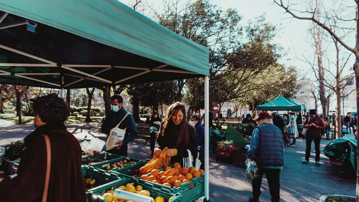 Shoppers choosing oranges and other produce at an outdoor farmers market in Lisbon
