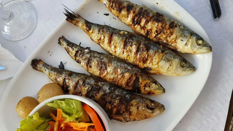 Whole grilled sardines served with boiled potatoes and salad on a white platter in Lisbon