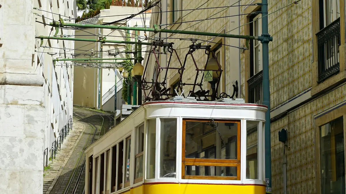 Yellow and white Lisbon funicular on steep rails beside a tiled building