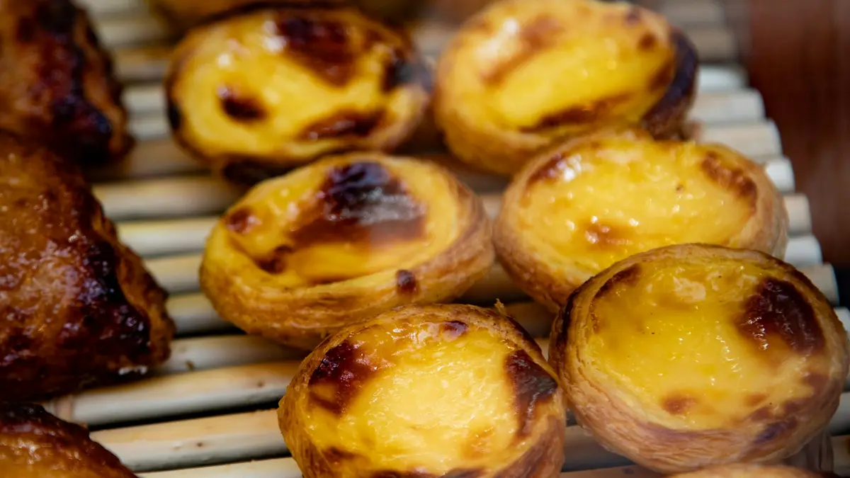 Pastéis de nata with flaky crusts and caramelized custard tops cooling on a metal rack in Lisbon