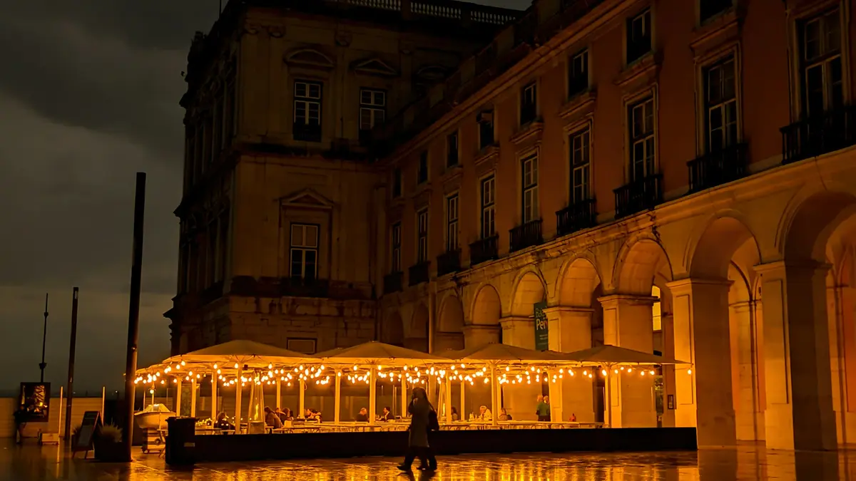 Wet Lisbon pavement reflecting café lights beneath a dark sky