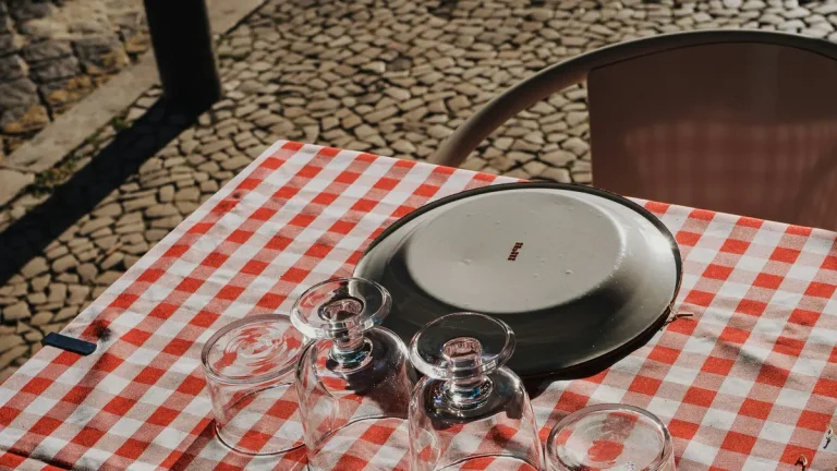 Red-and-white checked restaurant table with plates and glasses on Lisbon calçada pavement