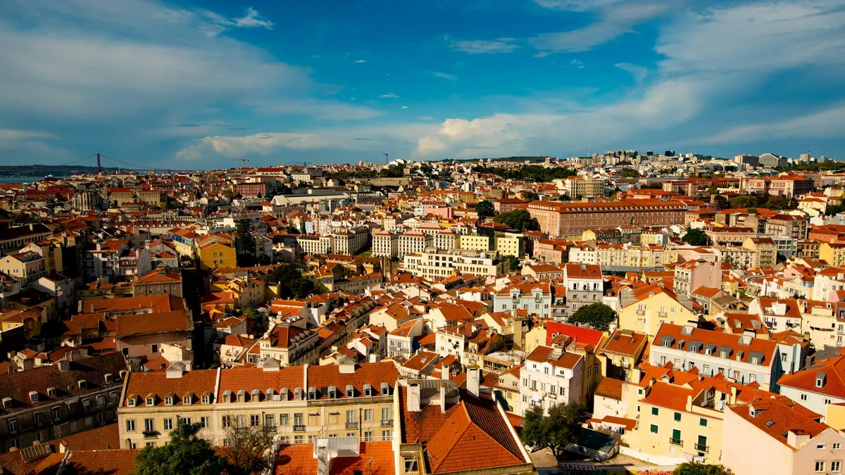 Sunlit Lisbon rooftops seen from Graça viewpoint beneath a blue sky with scattered clouds