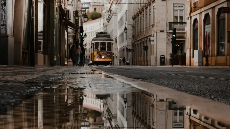 Historic yellow tram approaching on wet rails along a Lisbon street