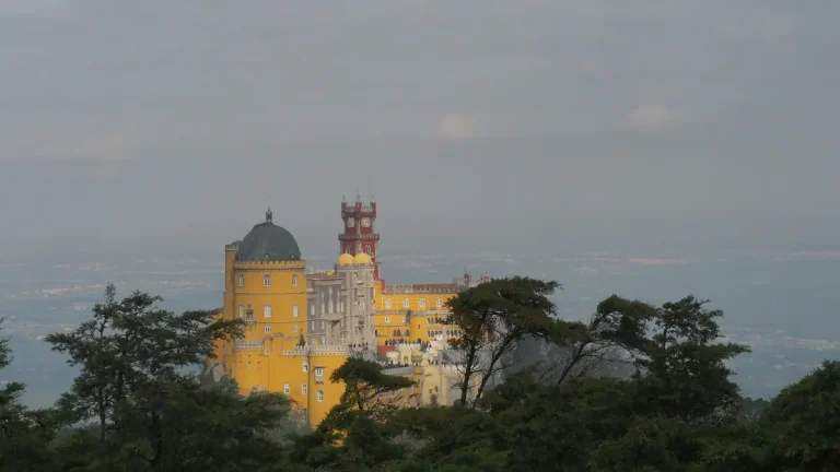 Yellow towers and a red turret of Pena Palace rising above the forested hills of Sintra