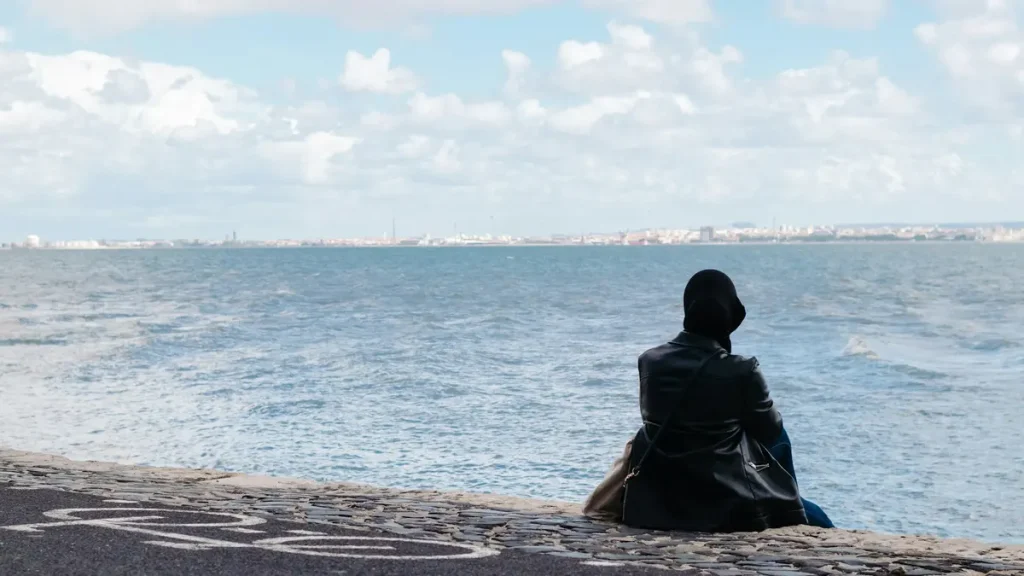 Person seated with their back to the camera beside the Tagus River in Lisbon