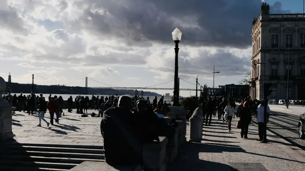 Backlit pedestrians crossing Praça do Comércio with the 25 de Abril Bridge beyond