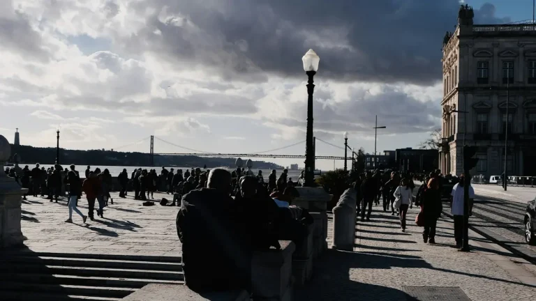 Backlit pedestrians crossing Praça do Comércio with the 25 de Abril Bridge beyond