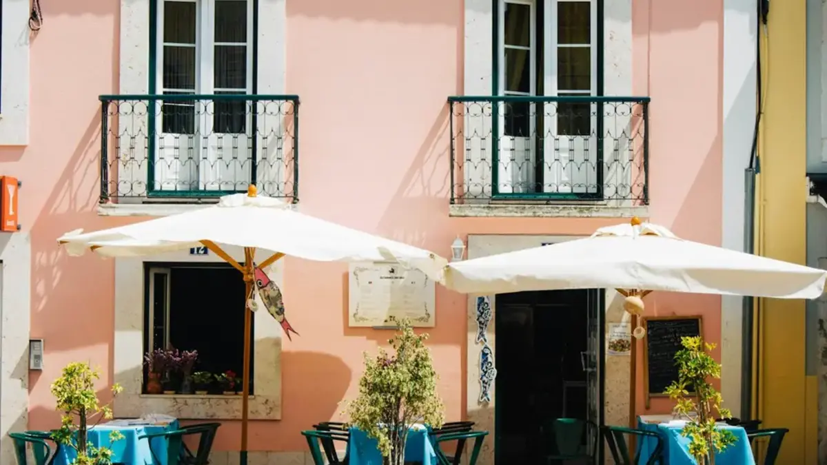Empty café tables beneath white umbrellas outside a pink building in Lisbon