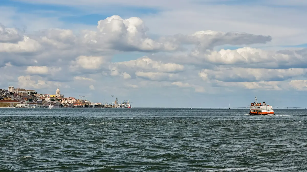 Orange and white passenger ferry crossing the Tagus River with Lisbon on the far shore