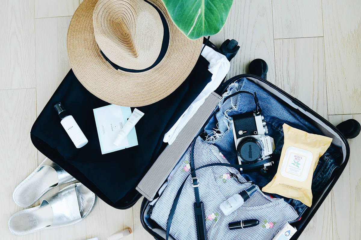 Open suitcase with sun hat, sunglasses and travel essentials laid out